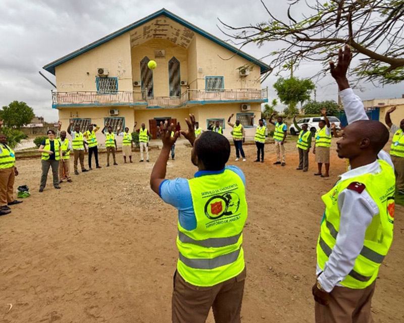 Group of individuals in yellow safety vests participating in disaster preparedness training outdoors, with a building in the background.