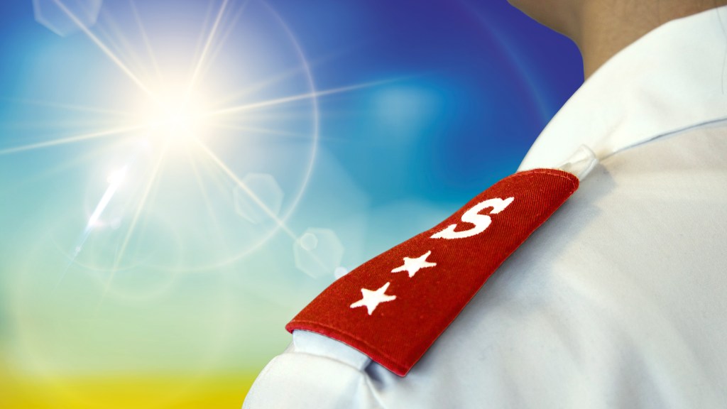 Close-up view of a Salvation Army uniform with a red epaulette featuring the letter 'S' and two stars, set against a bright, sunny backdrop.
