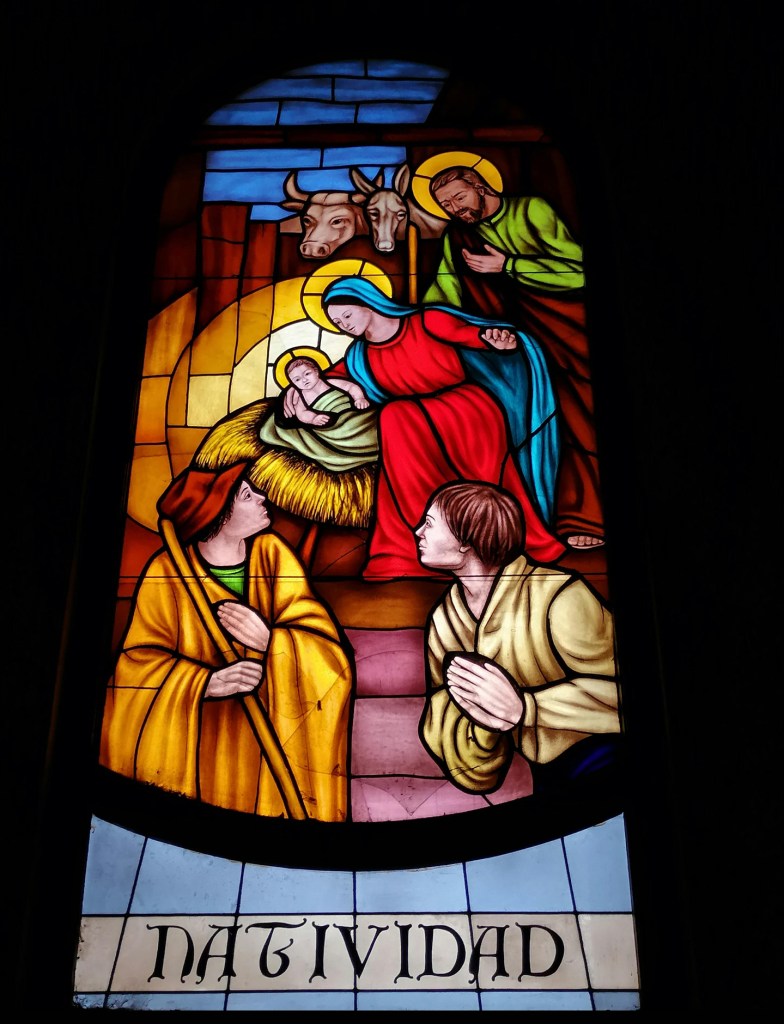 Stained glass depiction of the Nativity scene, featuring Mary, Joseph, and baby Jesus with animals and shepherds, highlighting the Christmas celebration.