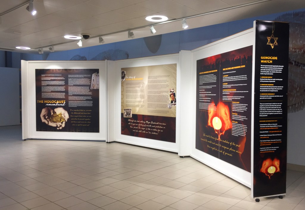 An exhibition space featuring informative panels about the Holocaust, including the title 'The Holocaust Remembered' and sections discussing genocide awareness and prevention.