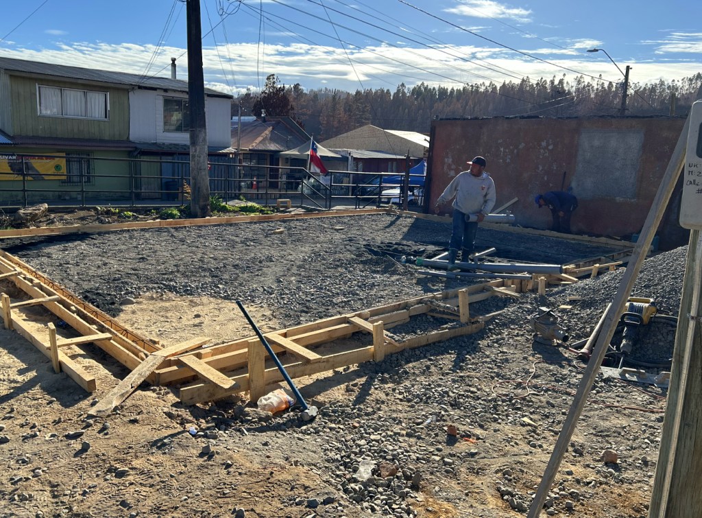 Construction workers preparing a gravel foundation marked by wooden framing in a residential area.