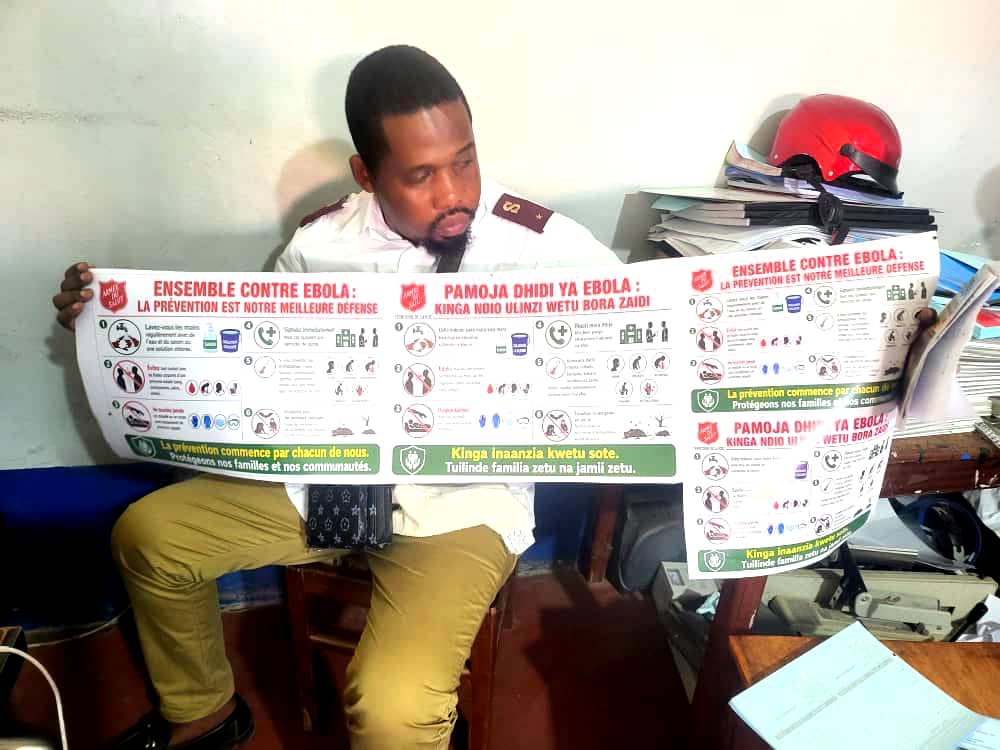 A man in Salvation Army uniform holds posters with Ebola information in different languages