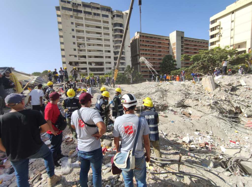 People in hard hats and Salvation Army t-shirts view a collapsed building