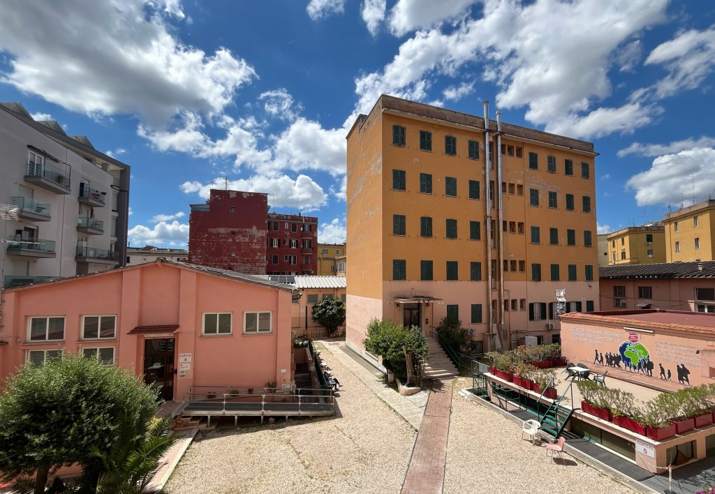 View of a courtyard surrounded by colourful residential buildings under a bright blue sky with scattered clouds.